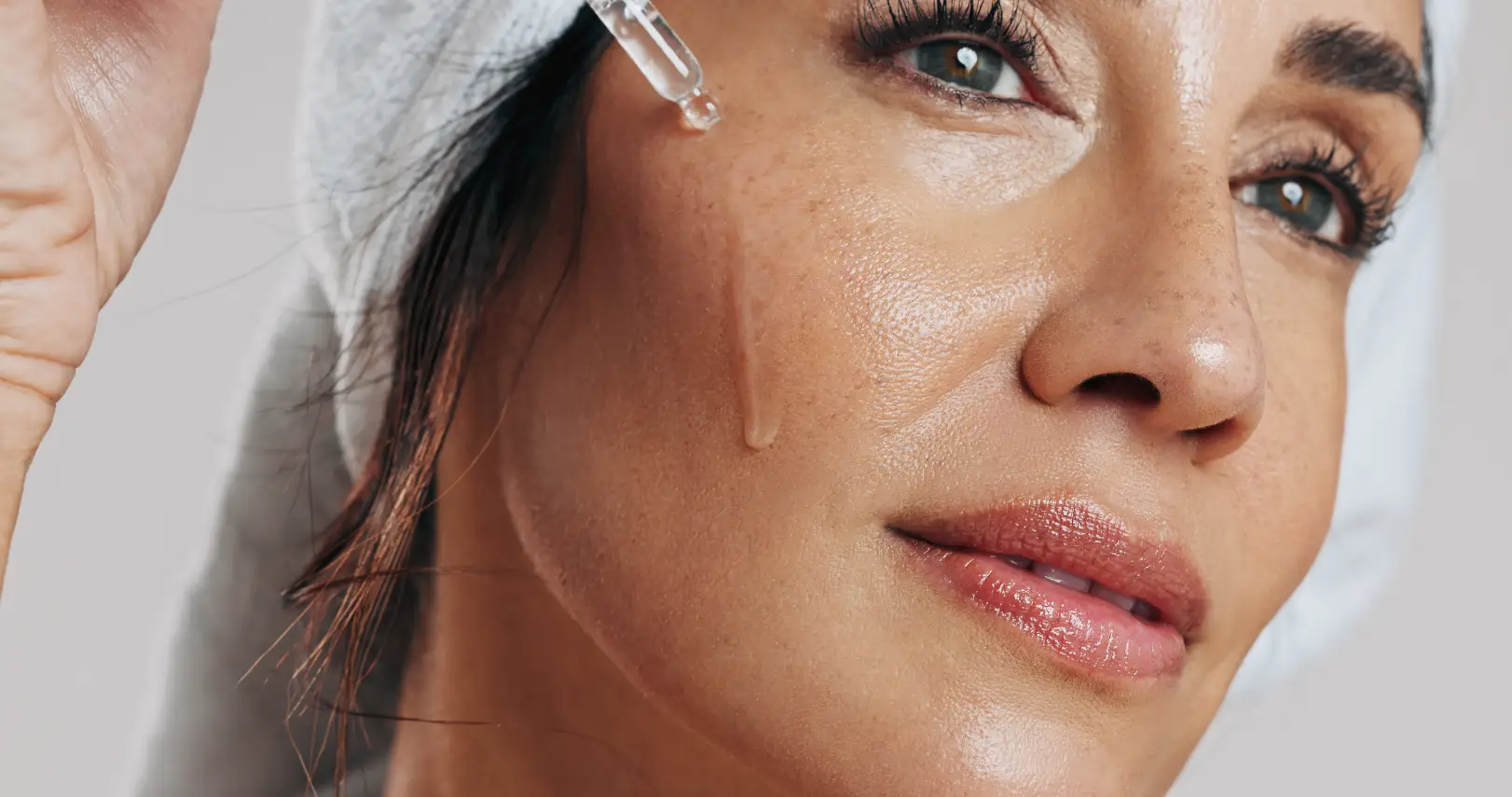 Close-up of a woman applying liquid serum to her cheek with a glass dropper.