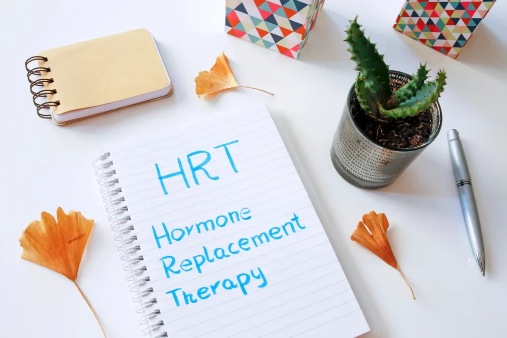 Open notebook with HRT and Hormone Replacement Therapy handwritten beside a potted plant and pen.